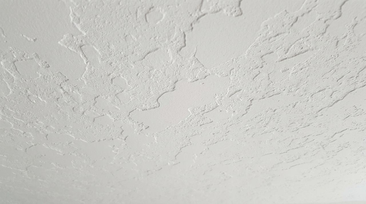 Wide taping knife drawing joint compound flat across a ceiling surface